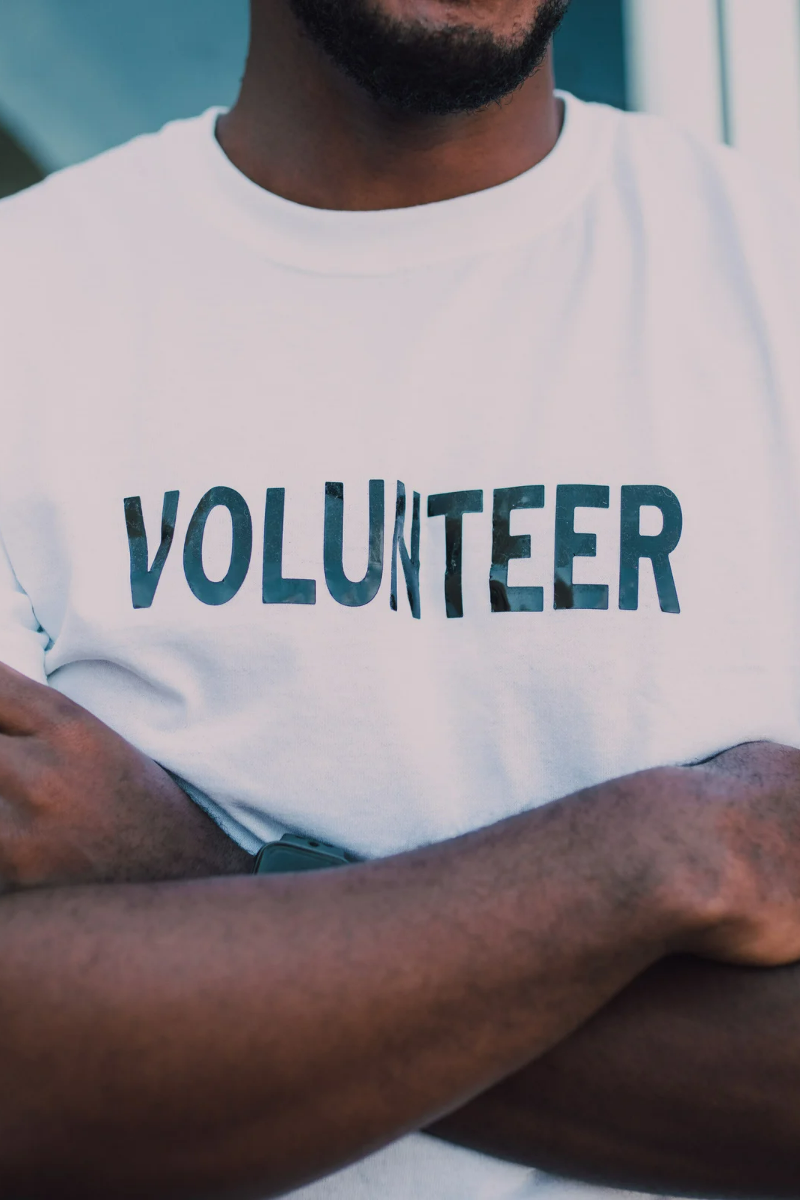 African American man standing with his arms crossed in a white tshirt that says volunteer across the chest in black.